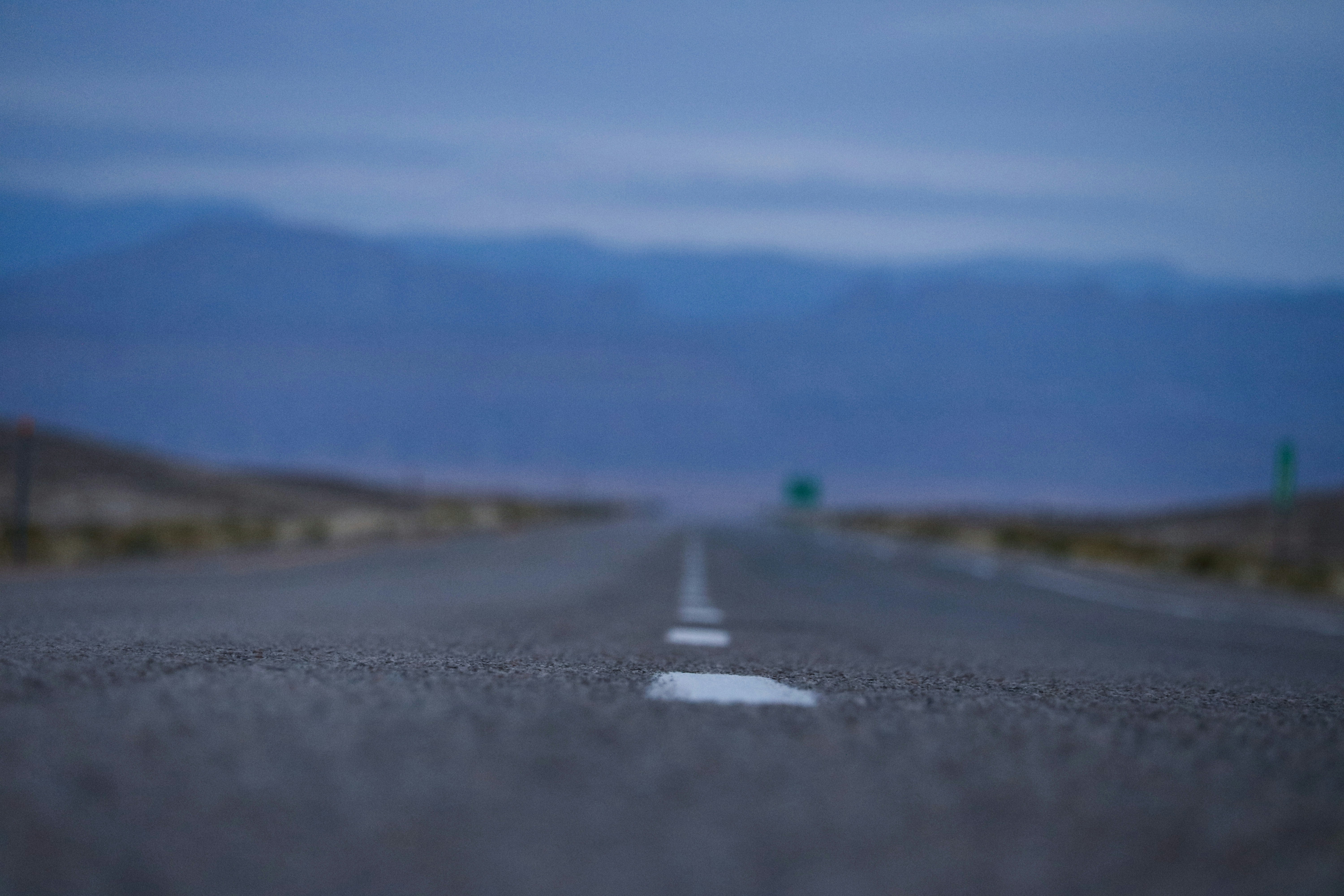 a ground-eye view, with the background blurred, of the white dashed line in the middle of a remote road