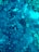 Aerial view of an underwater seafloor featuring rocks and clusters of coral or algae. The scene has a range of dark and light blue tones, with patches of green indicating marine life.