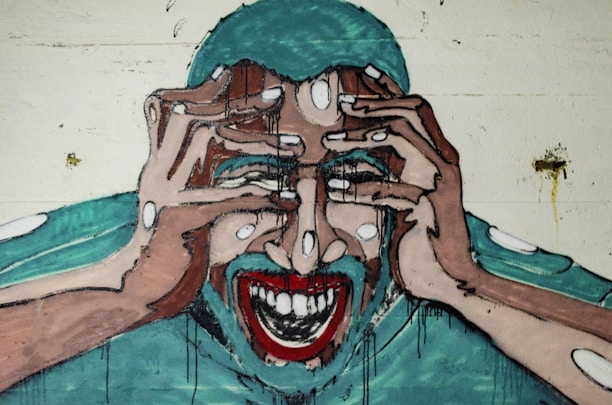 A graffiti-style mural depicts a person with their hands on their head, fingers interlaced, with a wide-open mouth showing teeth. The facial expression and posture suggest intense emotion or distress. The artwork is executed in a bold, stylized manner with thick lines and exaggerated features.