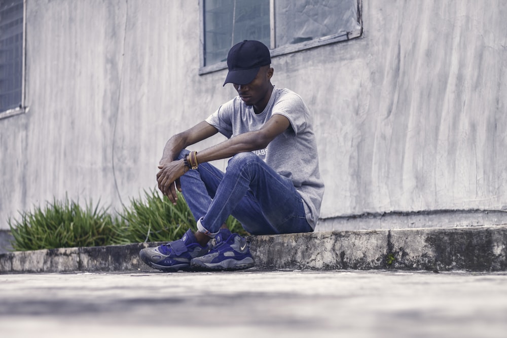 man in gray shirt sitting on concrete sideway