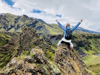 Woman standing on a mountain top with her arms raised in celebration, taking in the scenic view.