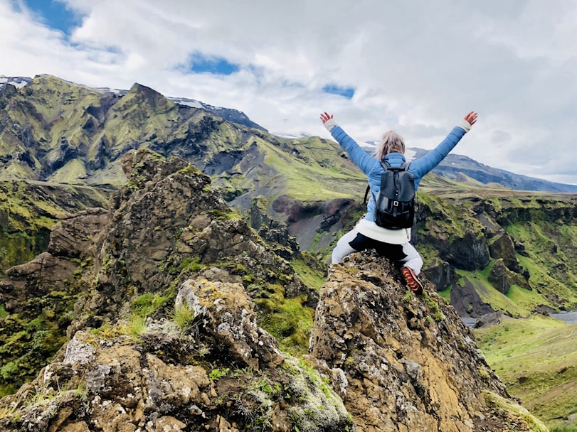 Woman standing on a mountain top with her arms raised in celebration, taking in the scenic view.