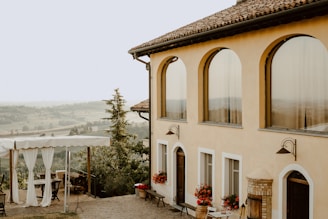 A sun-dappled stone terrace overlooking lush Italian countryside, draped with flowing cream curtains.