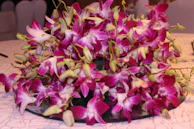 A sophisticated event table centerpiece featuring cascading orchids and lush foliage in muted tones.