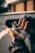 A hand holds a car key fob with shiny metallic parts, set against a blurred outdoor background, suggesting a vehicle in the surroundings.