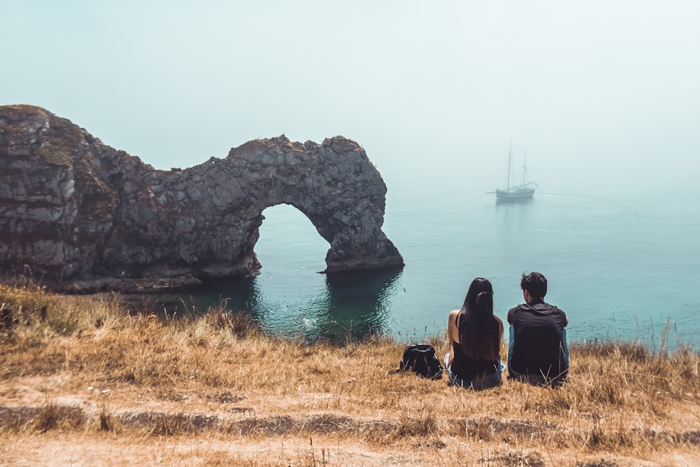 man and woman sitting beside rock formation