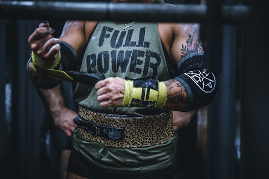 A focused powerlifter wearing a Strongbuild lever belt and wrist straps, chalking hands before a heavy lift in a gritty gym.
