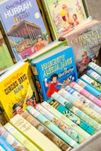 A collection of colorful children's books with illustrated covers, prominently featuring titles by Enid Blyton. The books are neatly arranged in a box, showcasing a variety of themes, including circus, adventure, and fantasy.