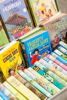 A collection of colorful children's books with illustrated covers, prominently featuring titles by Enid Blyton. The books are neatly arranged in a box, showcasing a variety of themes, including circus, adventure, and fantasy.