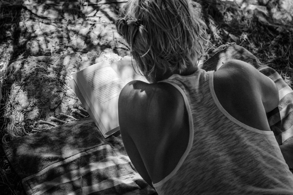 grayscale photo of man wearing razerback tank top reading book