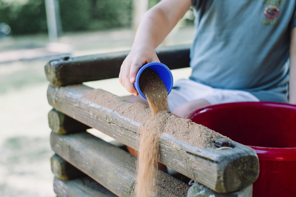 toddler pouring sand in brown wooden fence