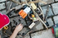 A child is playing with toy construction vehicles and wooden blocks on a cobblestone surface. There are sticks and dirt scattered around, and the child is engaging with the toys, possibly building or arranging something.