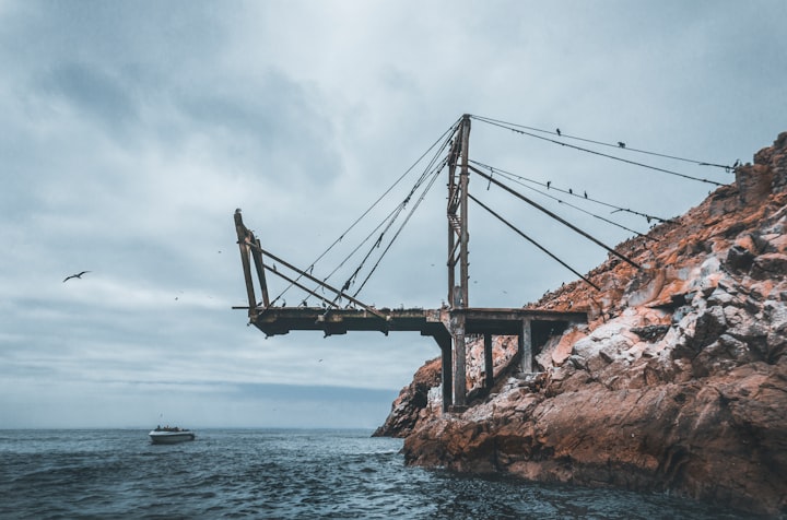 A metal bridge reaching out from a rocky shore and ending over open water under an overcast sky