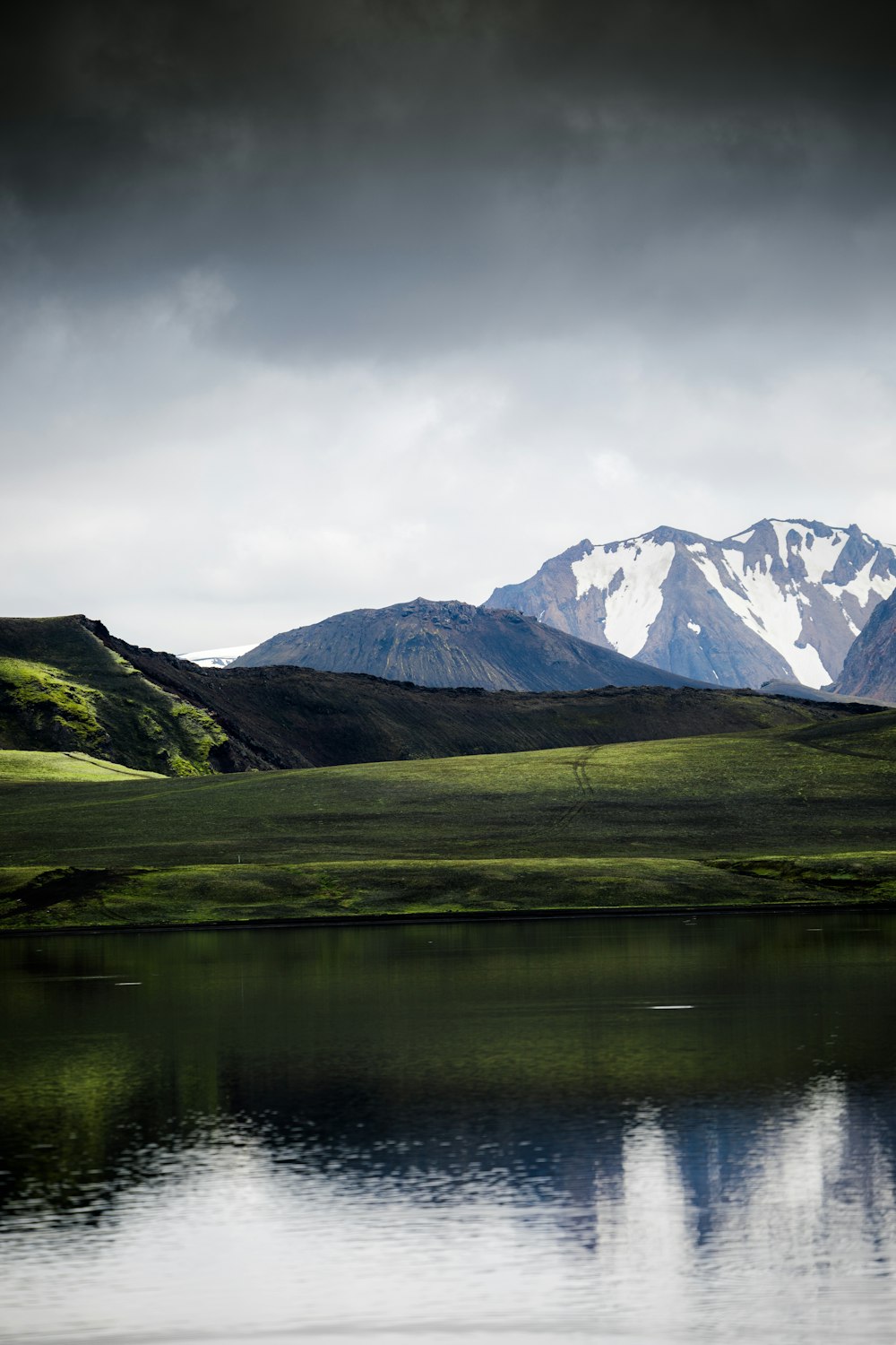 body of water beside hill grass and mountains at the distance