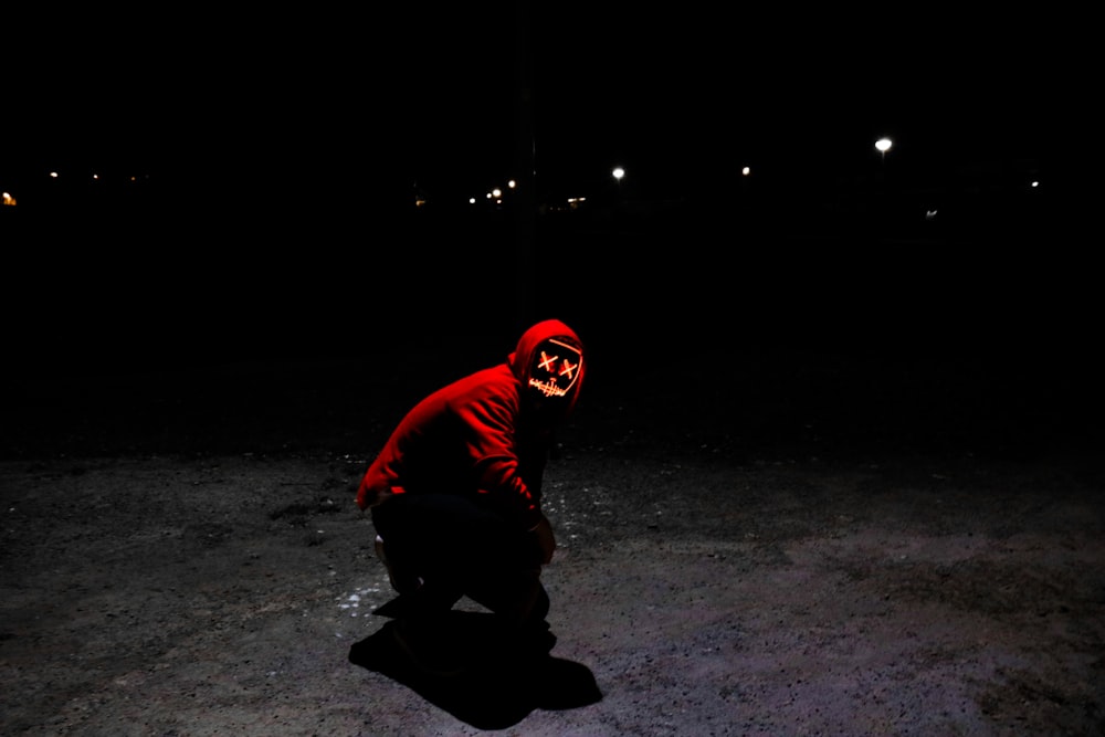 man wearing red hoodie squating on pavement