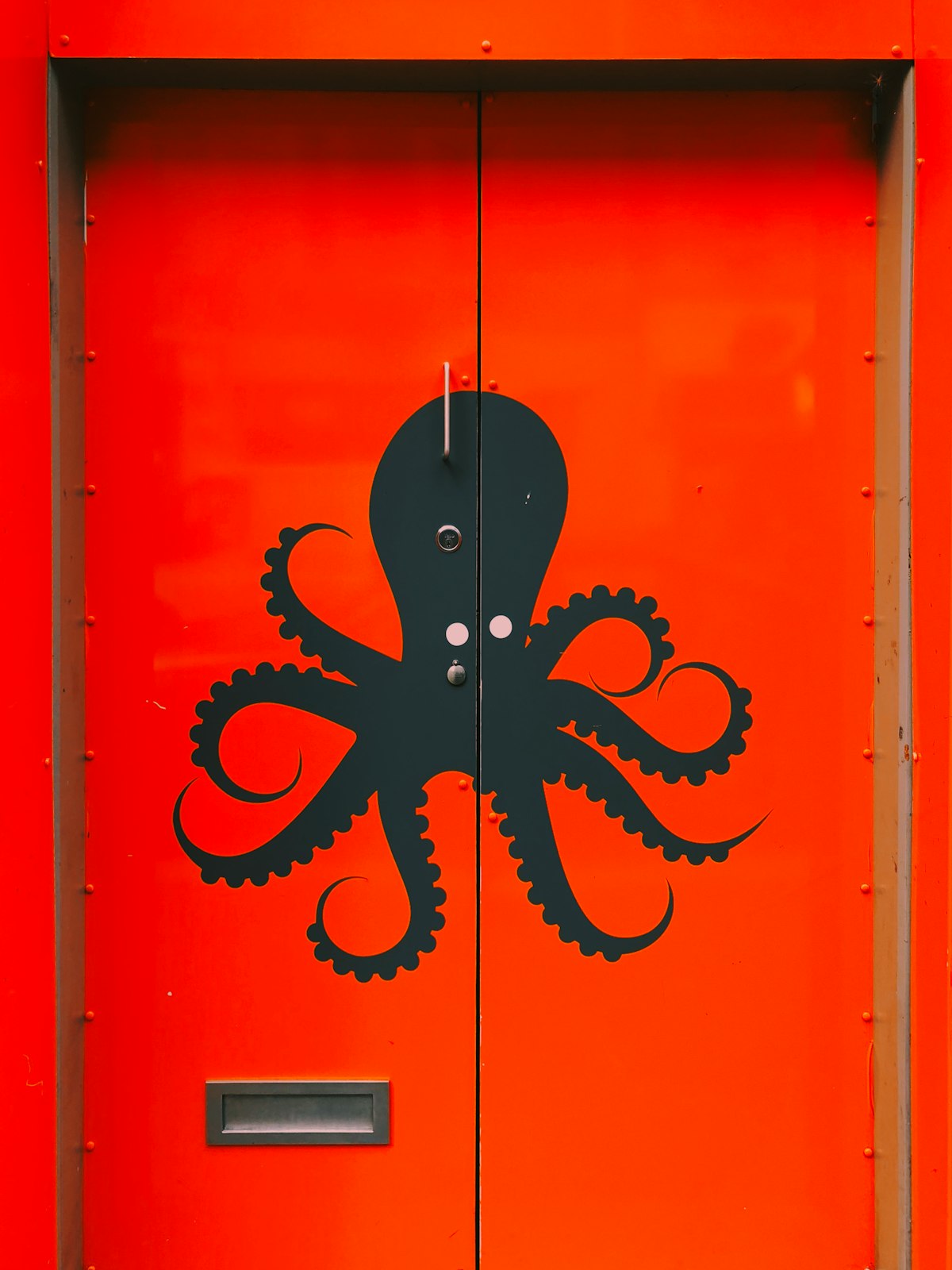 A black graphic of an octopus painted on a bright, red door.