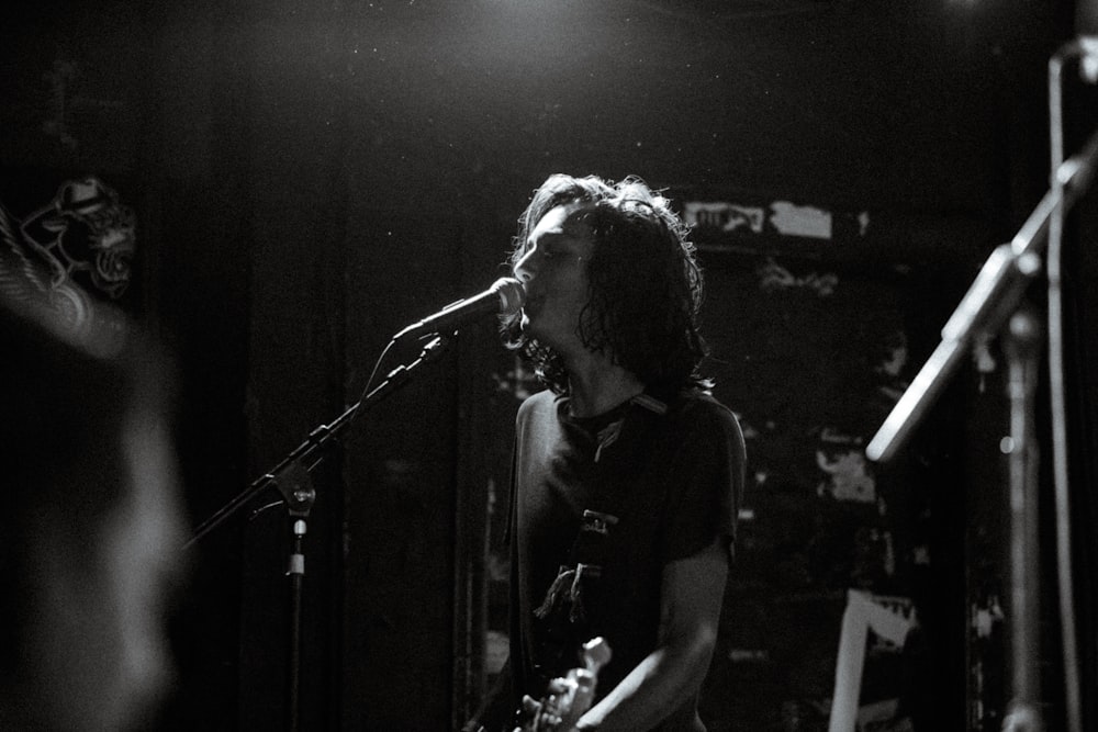 greyscale photo of man singing while holding guitar