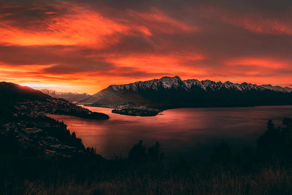 Breathtaking sunset over serene lake with mountain range in warm orange and red hues