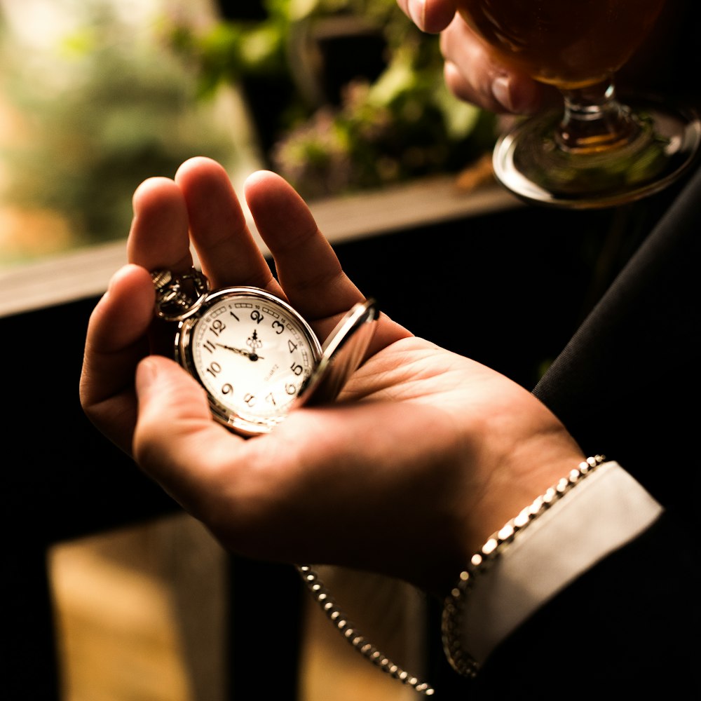 person holding silver-colored pocket watch