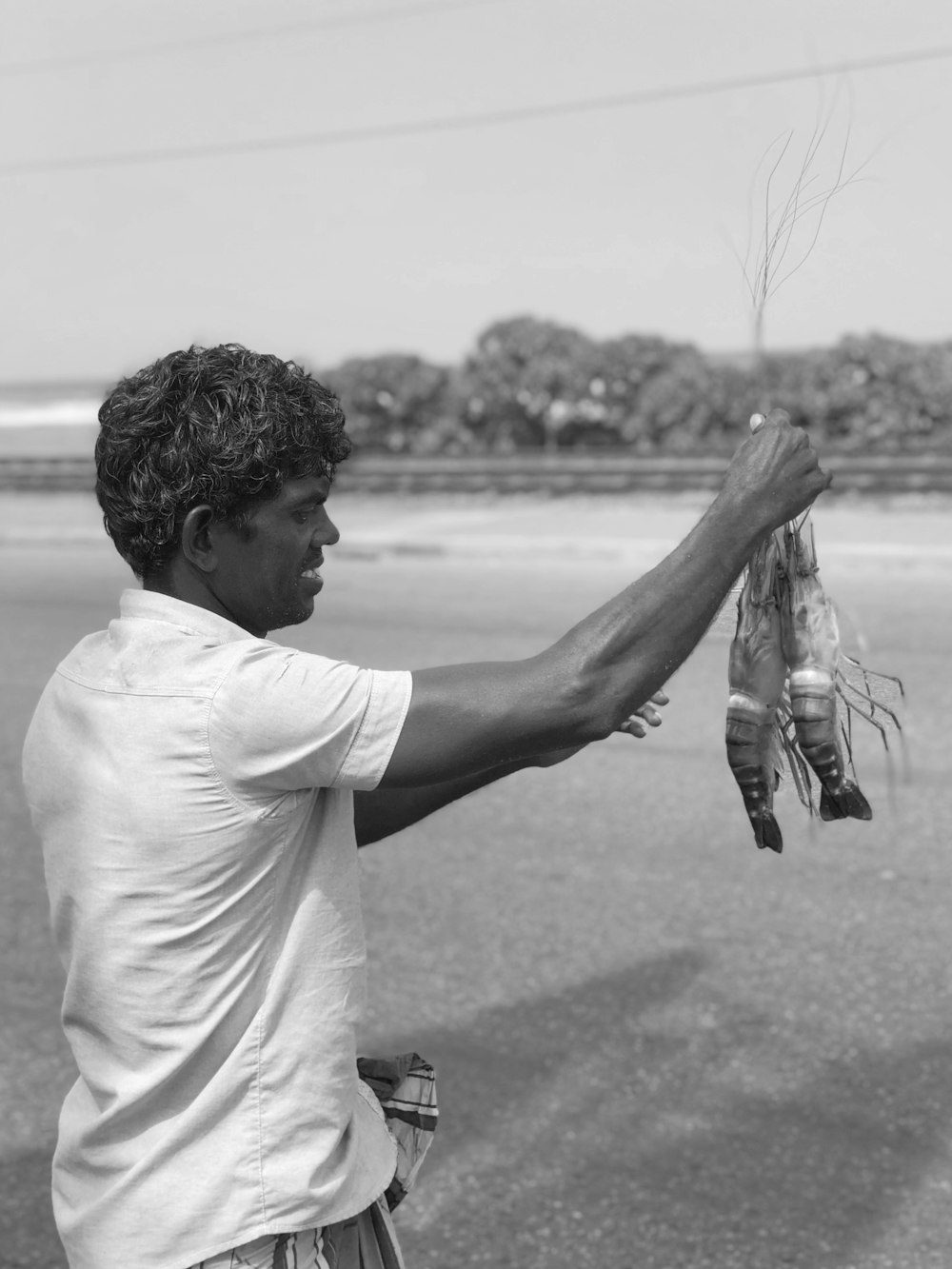 man holding shrimps on shore grayscale photography
