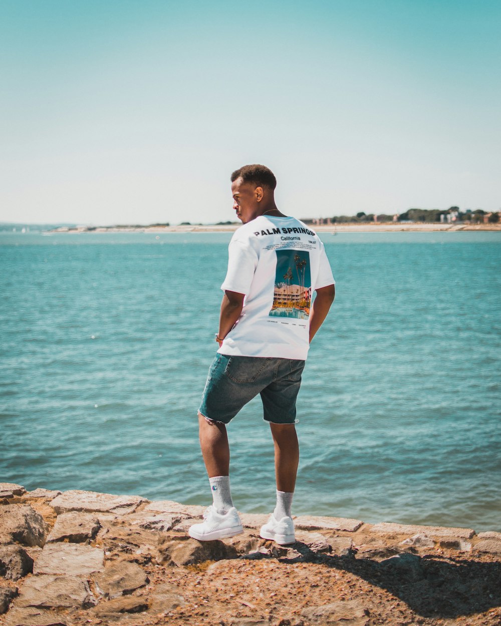 man standing on rock formation beside body of water