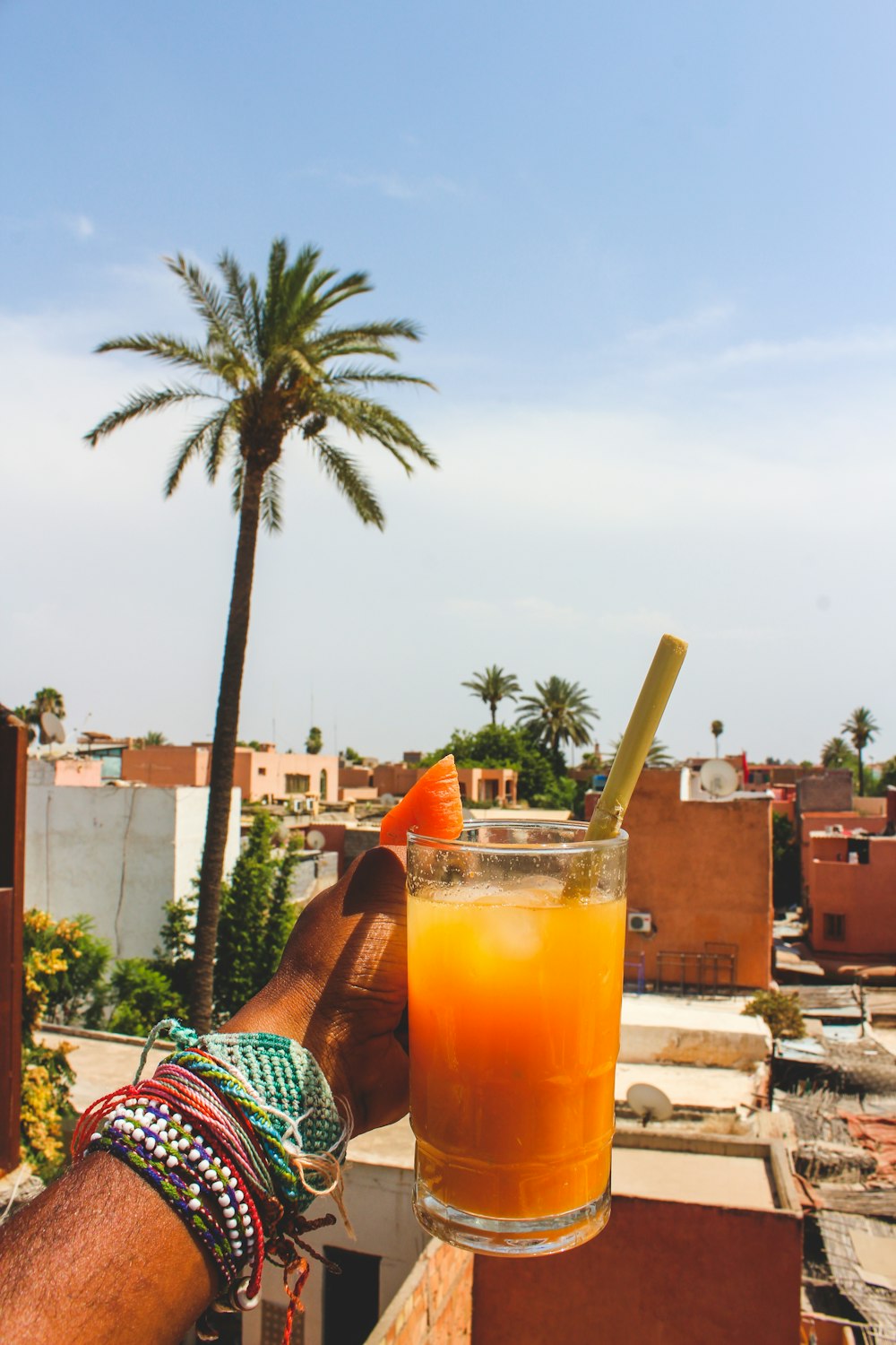 personne tenant une tasse en verre transparent avec un liquide orange