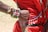 A close-up of an arm adorned with colorful bead bracelets, including one with the Kenyan flag design, rests on a person's back. The individual wears a red garment with decorative beads and metallic discs. The scene suggests cultural attire and craftsmanship.