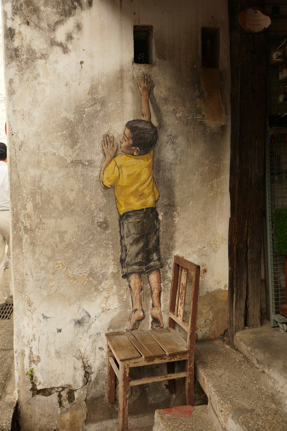 콘크리트 벽화에 구멍에 도달하는 나무 의자에 서있는 소년