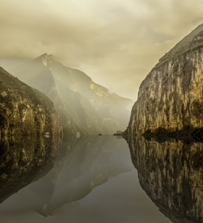 water between rocky mountain under white cloudy sky during daytime photo