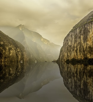 water between rocky mountain under white cloudy sky during daytime photo