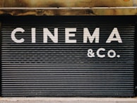 Large, bold white letters spell out 'CINEMA & CO.' on a black, corrugated metal shutter. The background appears industrial and slightly weathered, suggesting a closed or private cinema or entertainment venue.