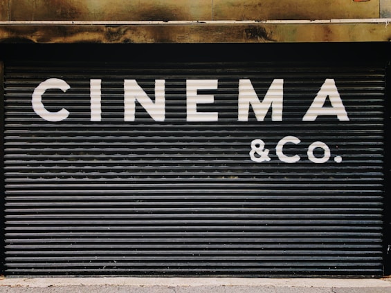 Large, bold white letters spell out 'CINEMA & CO.' on a black, corrugated metal shutter. The background appears industrial and slightly weathered, suggesting a closed or private cinema or entertainment venue.