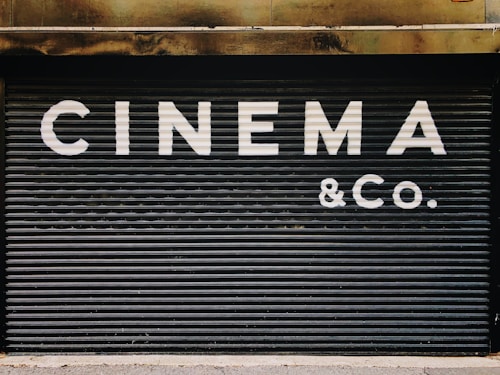 Large, bold white letters spell out 'CINEMA & CO.' on a black, corrugated metal shutter. The background appears industrial and slightly weathered, suggesting a closed or private cinema or entertainment venue.