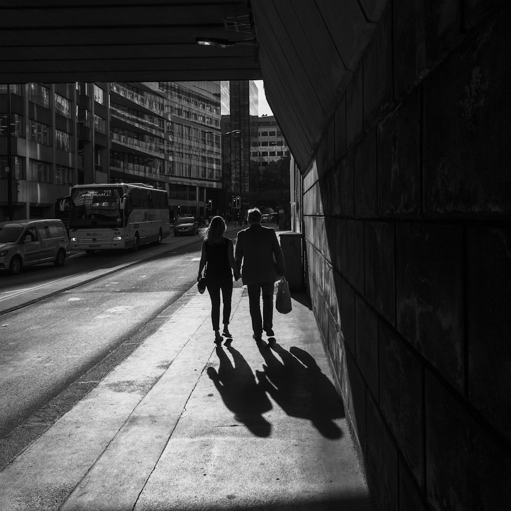 grayscale photography of man and woman walking on sidewalk