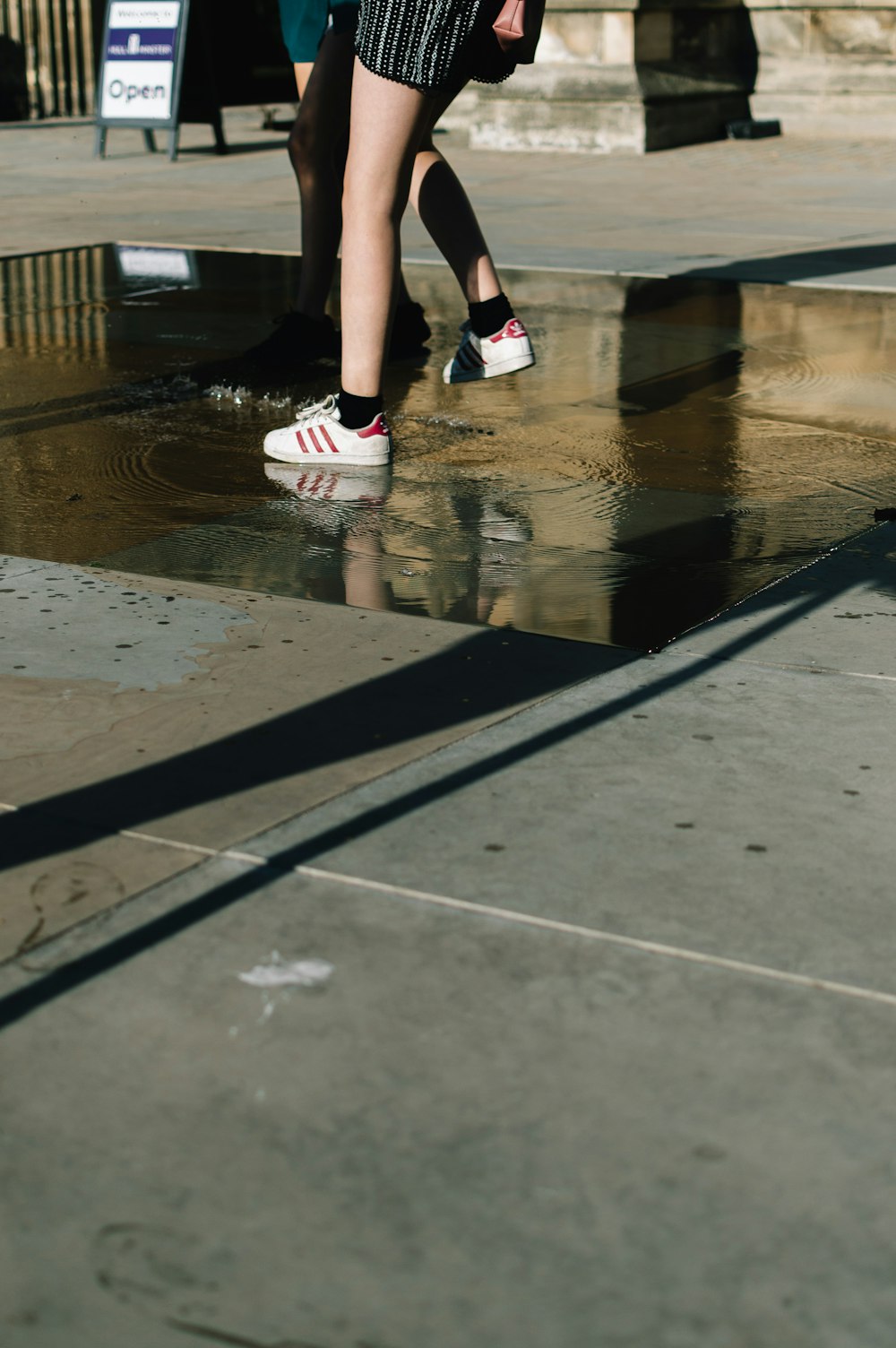 person wearing white-and-red adidas sneakers stepping on puddle of water