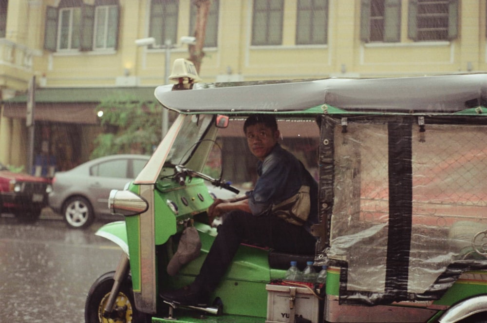 a man driving a small green vehicle down a street