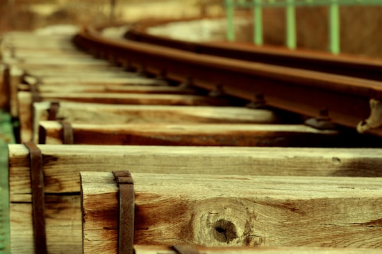 A close-up view of wooden railway tracks stretching into the distance. The focus is on the texture of the wooden beams, with the metal rails curving gently as they extend out of view.