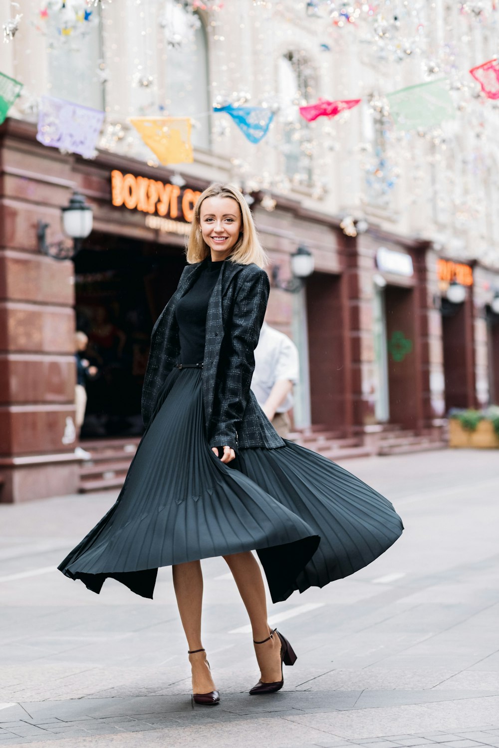 photo de mise au point sélective d’une femme souriante portant une robe noire debout sur un trottoir en béton