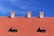 A red-tiled roof with two small dormer windows and three brick chimneys under a clear blue sky.