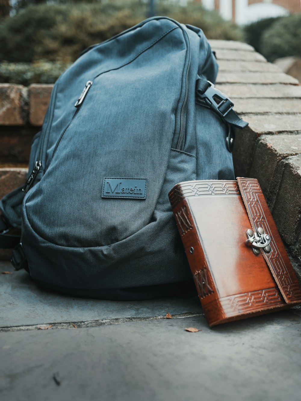 brown leather briefcase and gray Matein bag on concrete slab