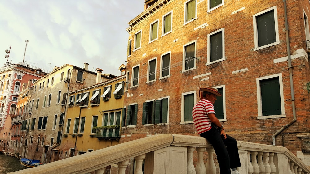 person sitting on concrete handrail near canal during daytime