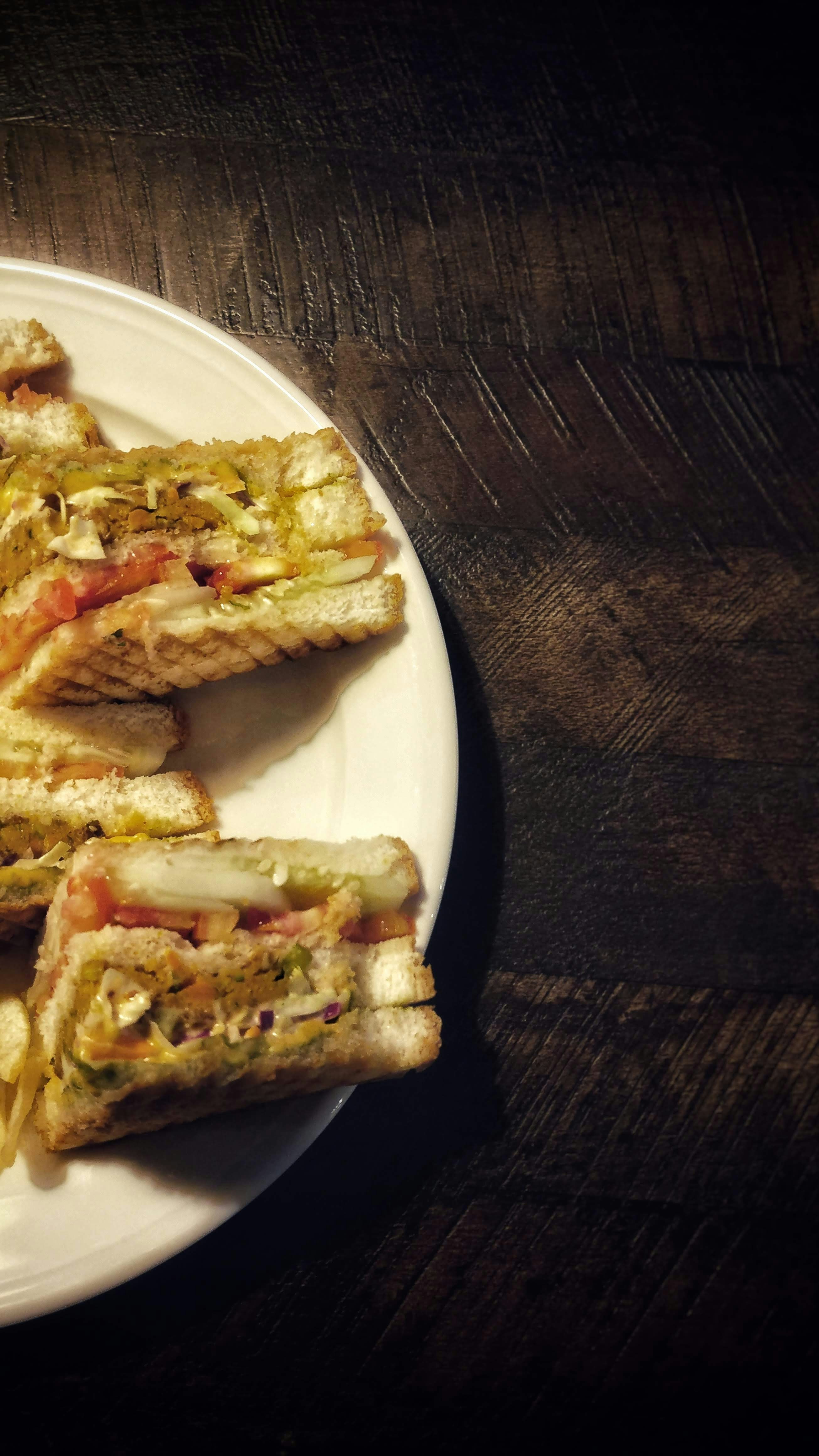 Grilled club sandwich cut diagonally with layers of cheese and vegetables on dark surface, soft ambient lighting