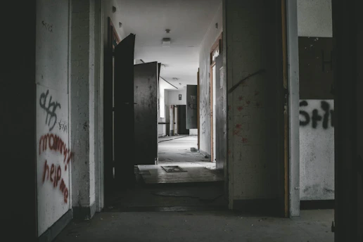 A dimly lit abandoned corridor lined with weathered investigation files and scattered old photographs pinned to a corkboard.