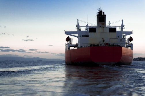A cargo ship navigating through calm waters at sunset.