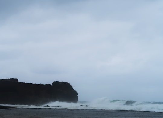 white seawaves near silhouette rock formation under white cloudy sky at daytime in Ilocos Norte Philippines