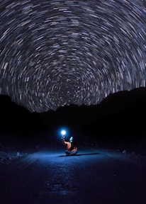 photo of person sitting on pave road holding light