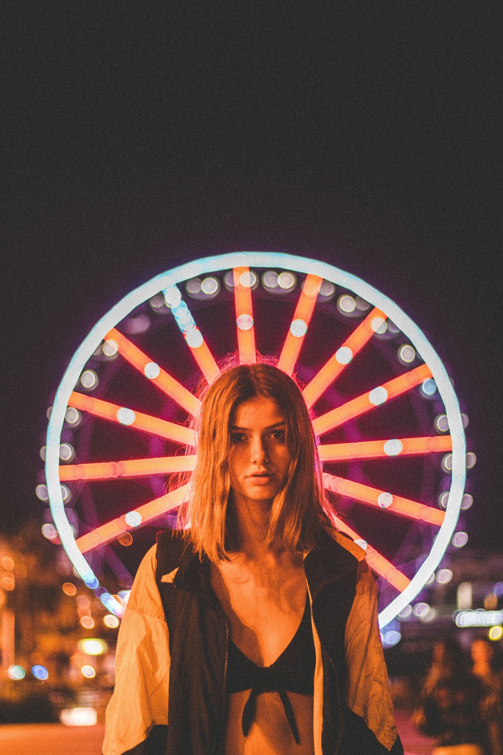 woman standing in front of lighted Ferris wheel at nighttime