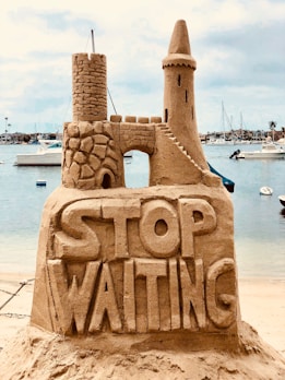 Sandcastle with ‘STOP WAITING’—Redurb Dream Guides inspires reflection and dream exploration.