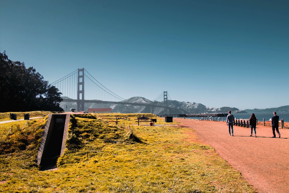 mens and woman walking near bridge and mountain at daytime