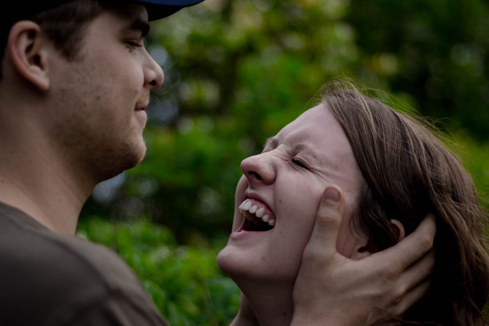 man holding the face of woman smiling near plants at daytime